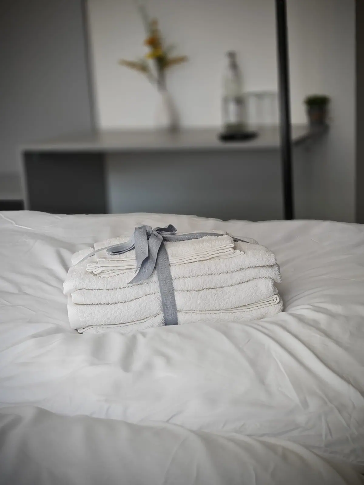 Mit grauem Band gebundener Handtuchstapel auf frisch bezogenem Bett